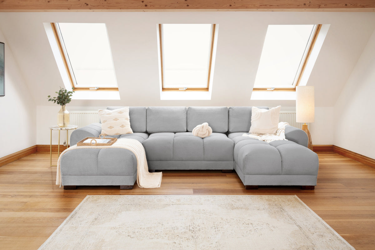 Gray sectional sofa in a living room with wooden floor and skylights.