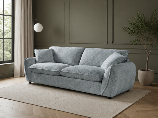 A light gray upholstered loveseat sofa with two matching throw pillows, styled in a modern living room setting with a beige rug, wood paneled walls, a window, and a potted plant.