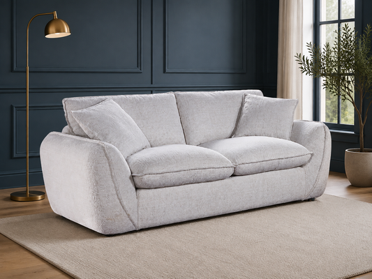 A light beige upholstered loveseat with two loose back cushions and two seat cushions, shown in a styled room with a dark blue paneled wall, a gold floor lamp, a beige rug, and a potted plant.