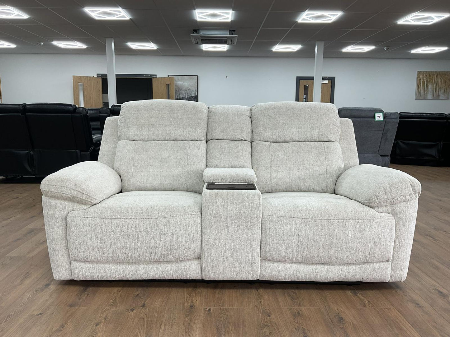 beige reclining sofa in a showroom setting with wooden flooring and ceiling lights.