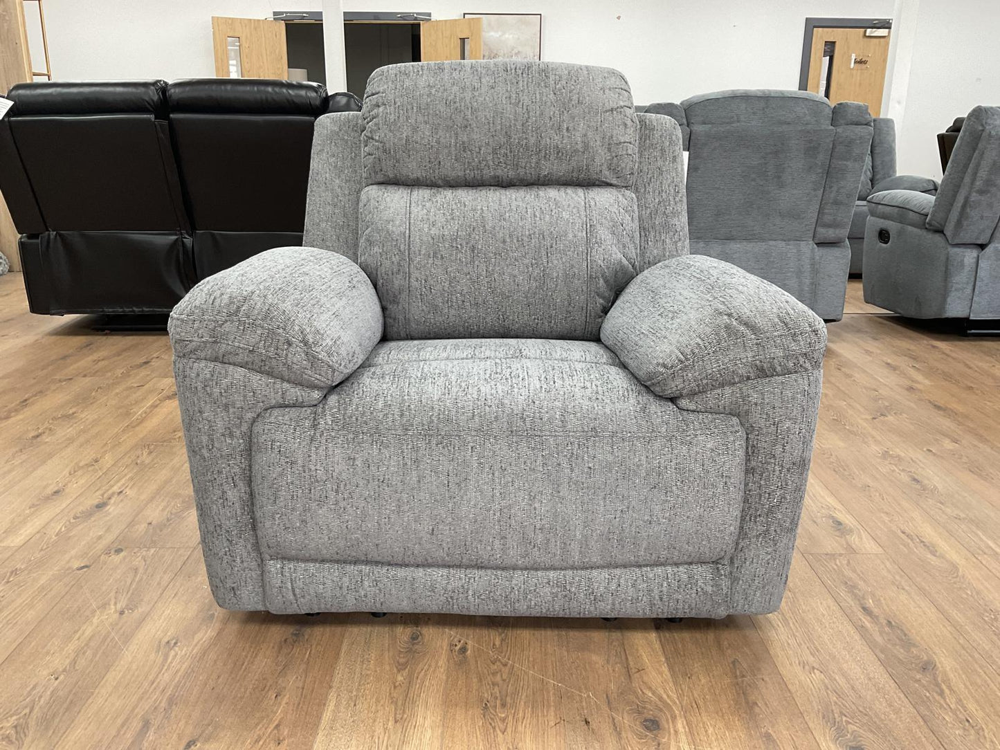 Gray recliner chair in a showroom setting with other furniture in the background.