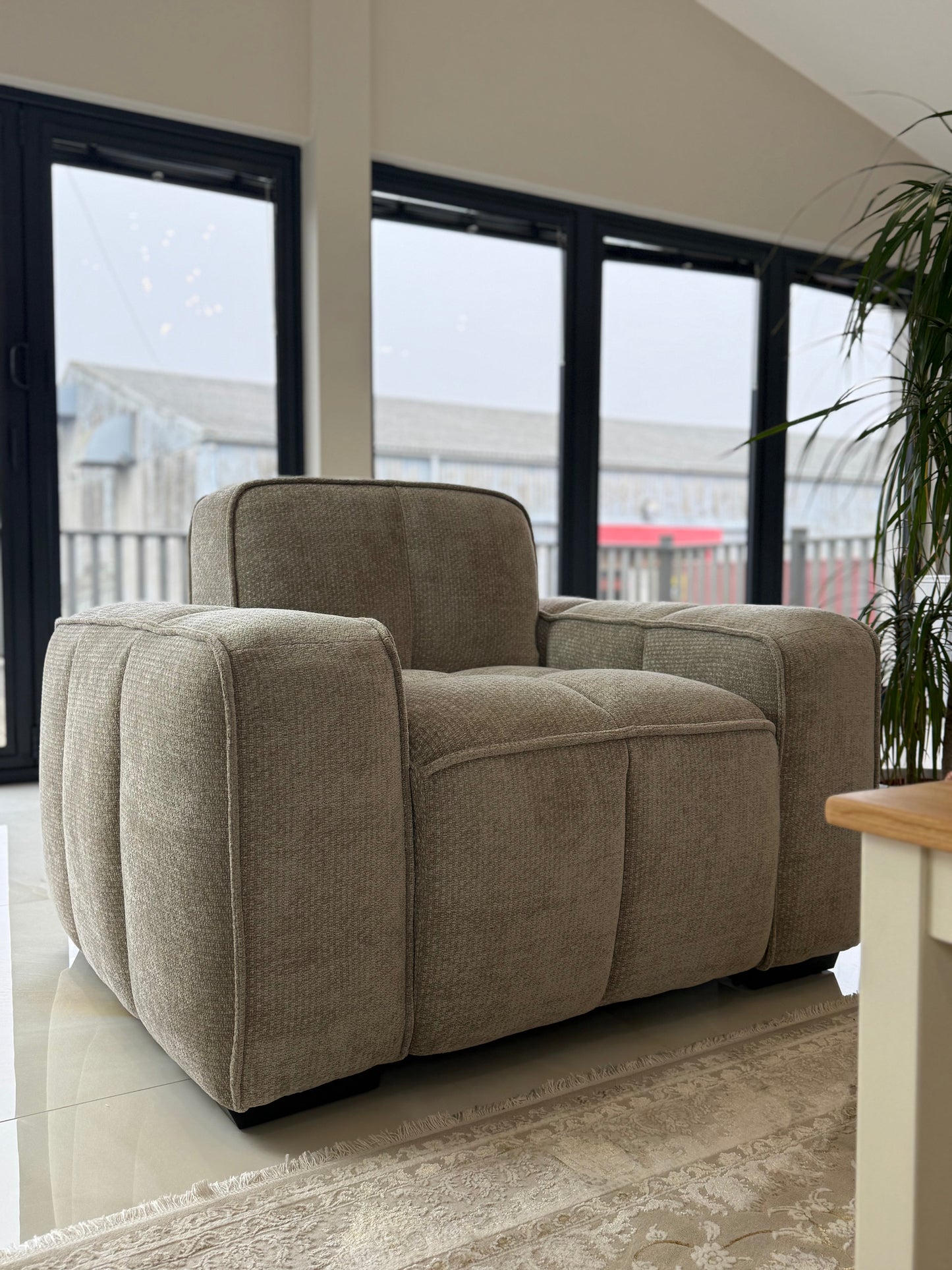 Beige armchair in a living room with large windows and a plant.