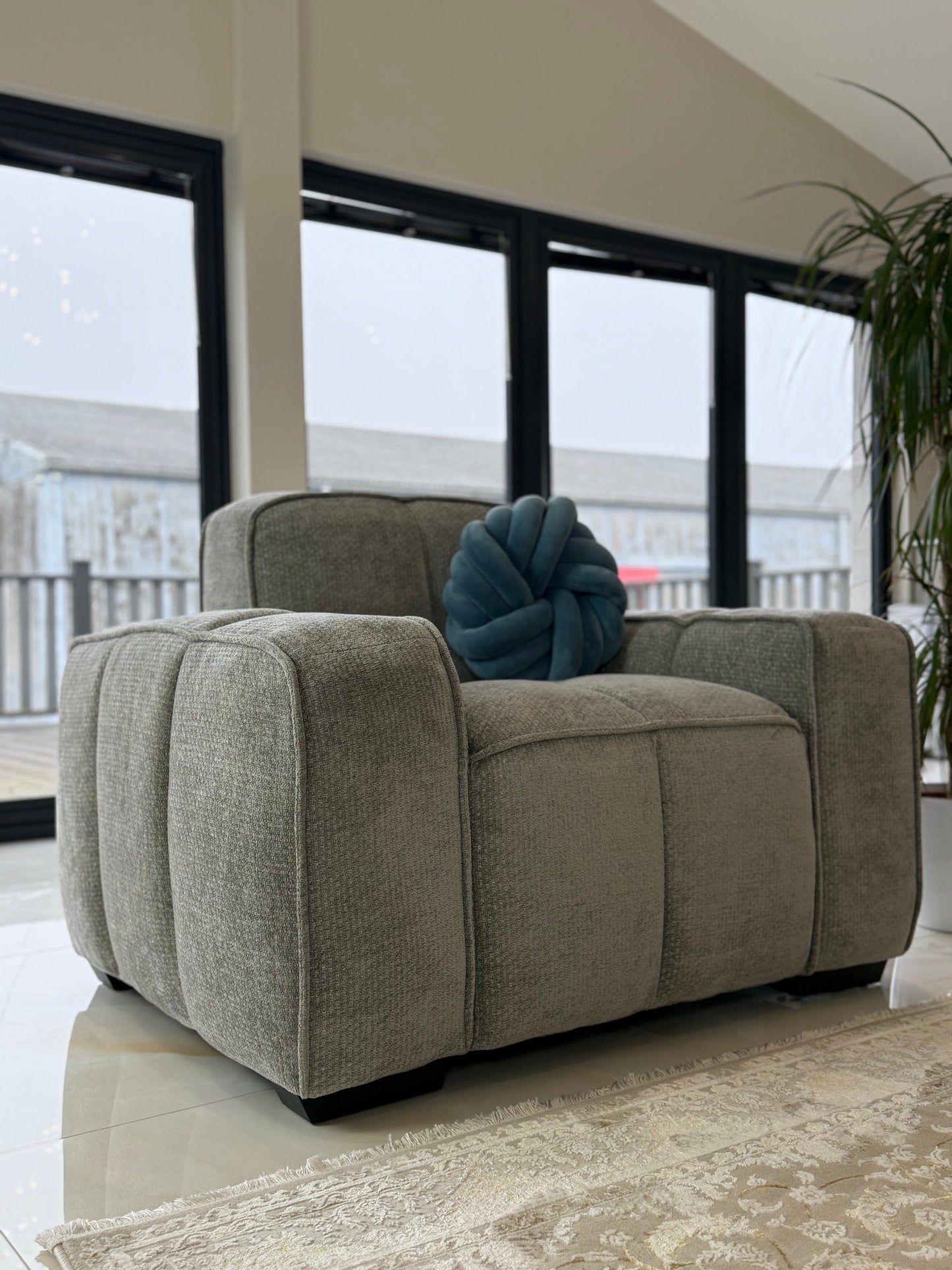 Gray armchair with a blue cushion in a room with large windows.