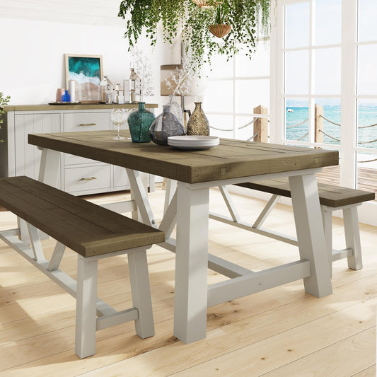 Wooden dining table with benches in a bright room with large windows overlooking water.