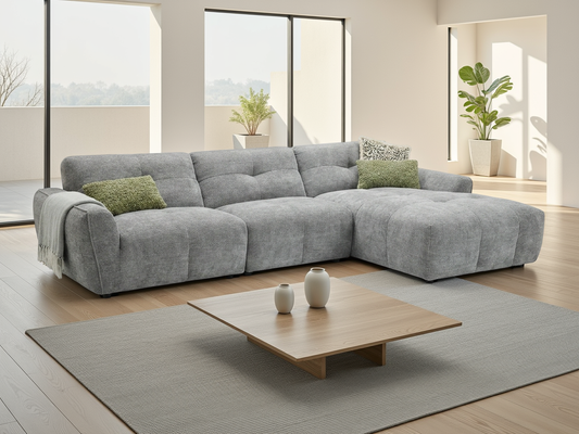 A modern light gray fabric sectional sofa with tufted cushions and two green accent pillows.