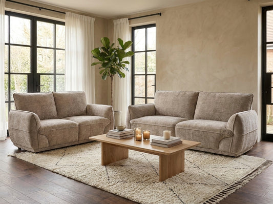 A staged living room featuring a light beige upholstered loveseat and matching sofa set with a wooden coffee table and a large textured area rug.
