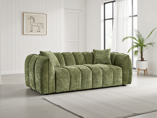 Green sofa in a room with a plant and framed picture on the wall.