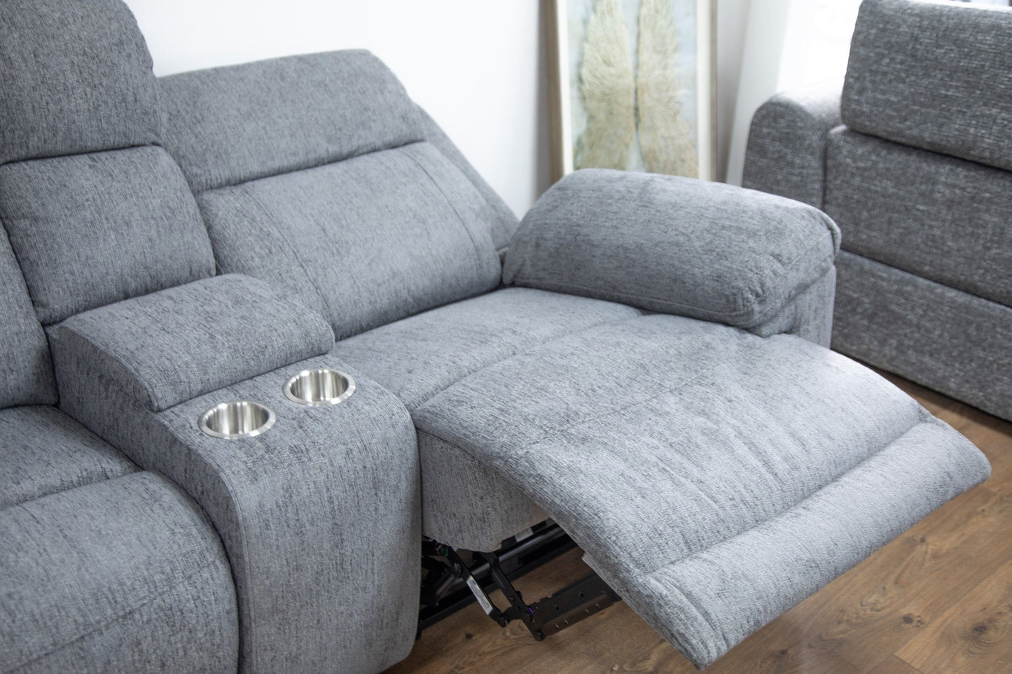 Gray recliner sofa with cup holders on a wooden floor.