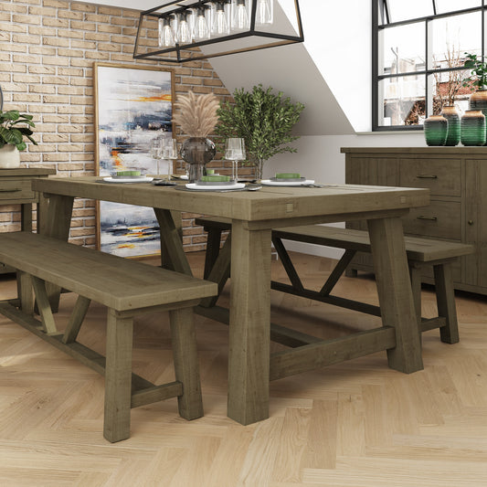 Wooden dining table with benches in a room with a brick wall and large window.