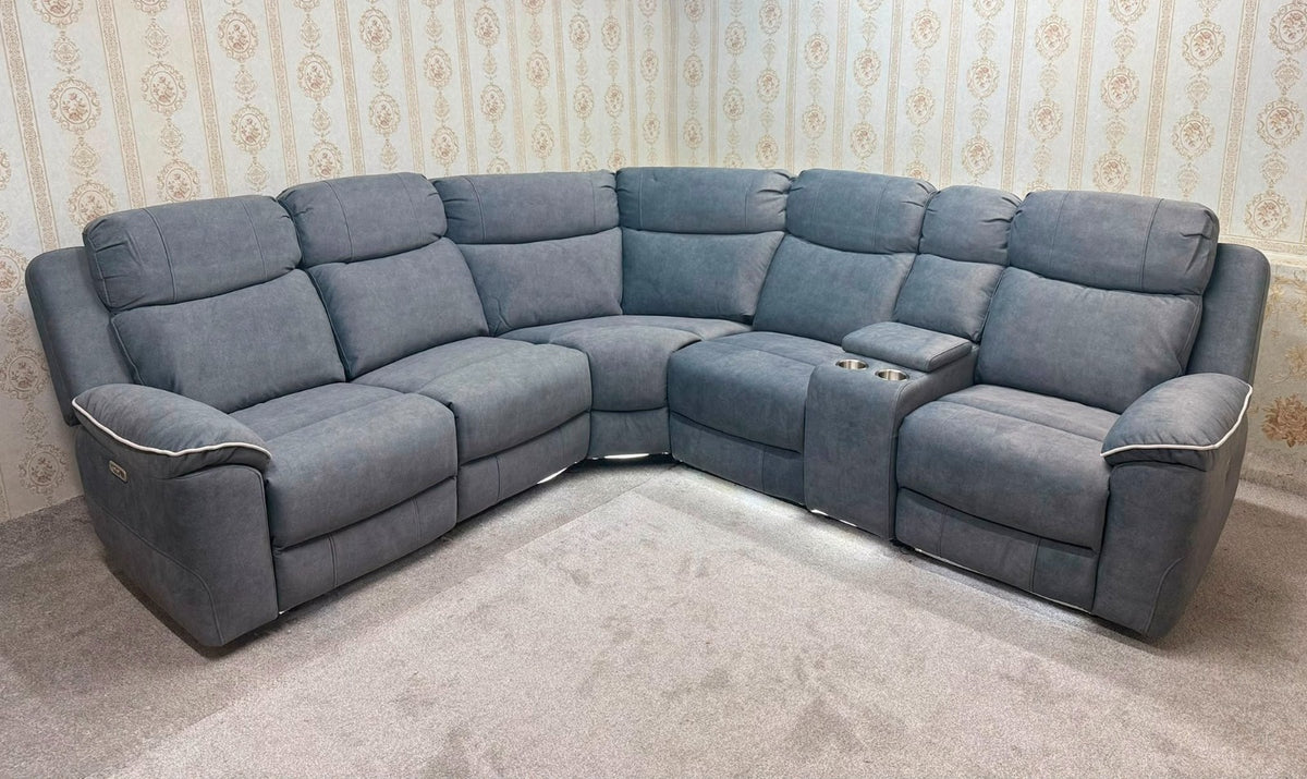 A large L-shaped modular recliner sofa in a dusty blue-gray fabric, positioned in a room with patterned wallpaper and a light-colored carpet.