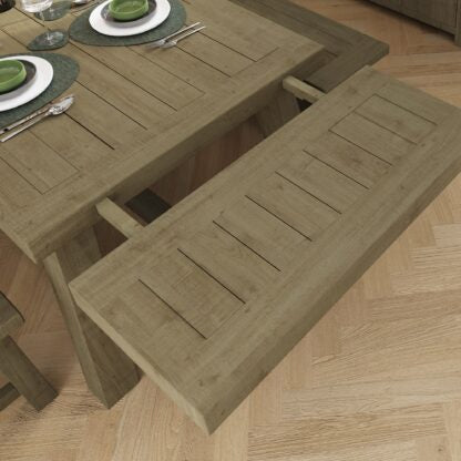 A rustic wooden dining table with matching slatted benches, shown in a real interior setting with a light wood floor and place settings on the tabletop.
