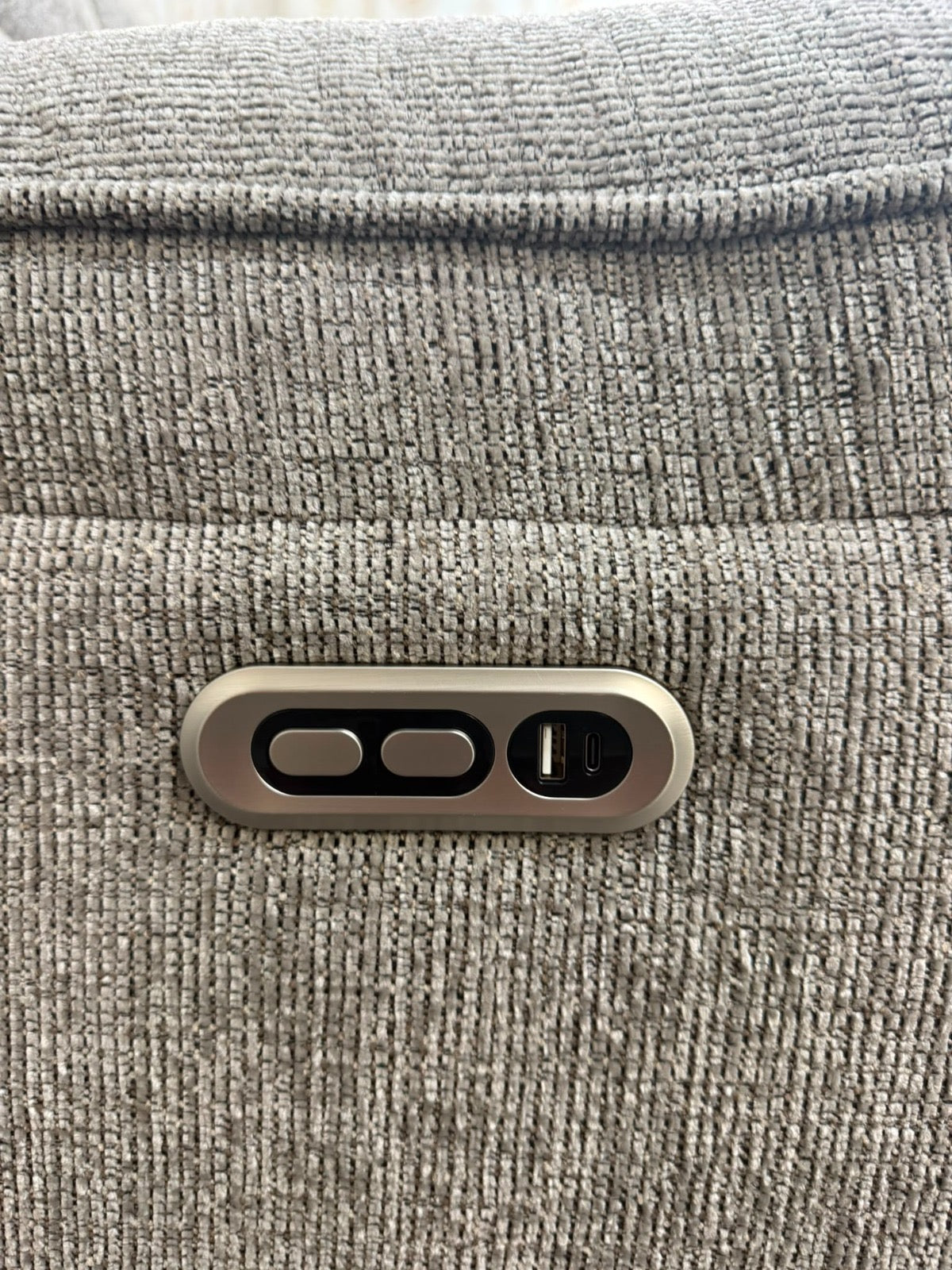 Close-up of a metallic control panel with three buttons and a small display, mounted on a textured gray fabric surface.