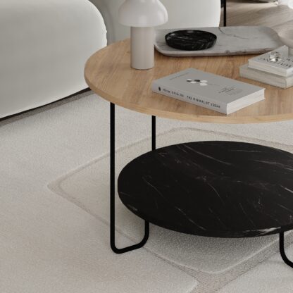 A modern round coffee table with a light wood top, a black marble-patterned lower shelf, and thin black metal legs, styled in a minimalist living room setting.