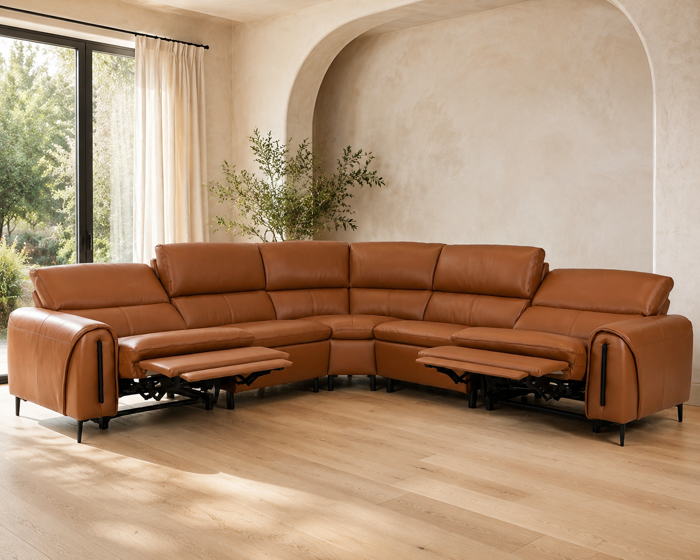 A large sectional sofa upholstered in warm tan leather, shown in a staged living room with wood flooring, cream walls, and large windows.