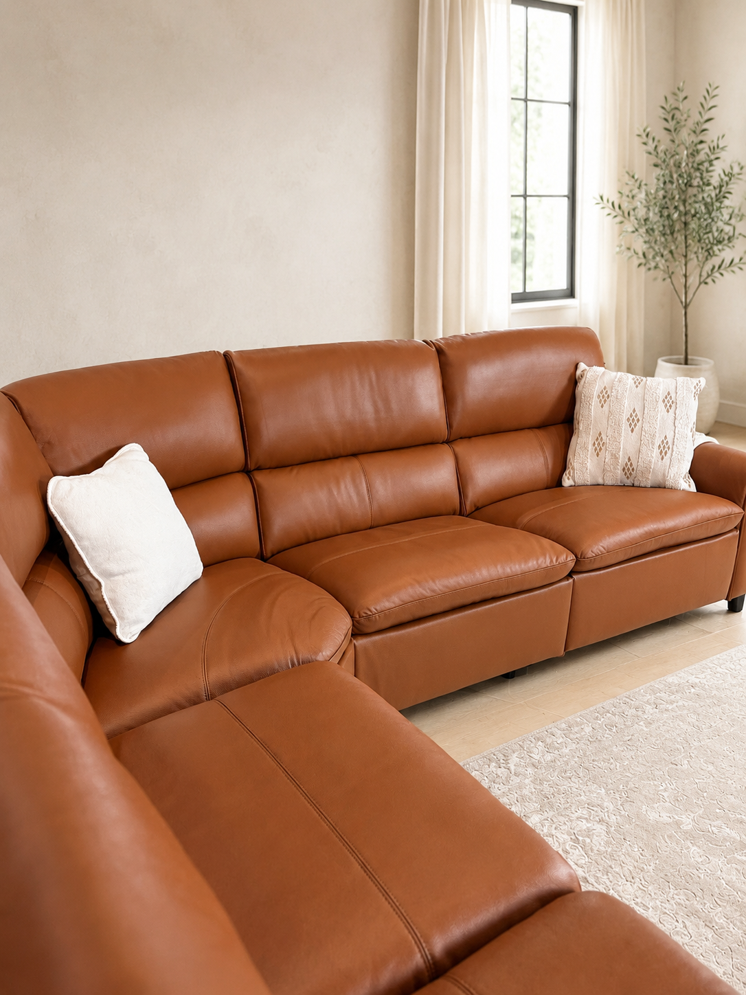 A modern large sectional corner sofa upholstered in warm cognac brown leather, in a bright, contemporary living room.