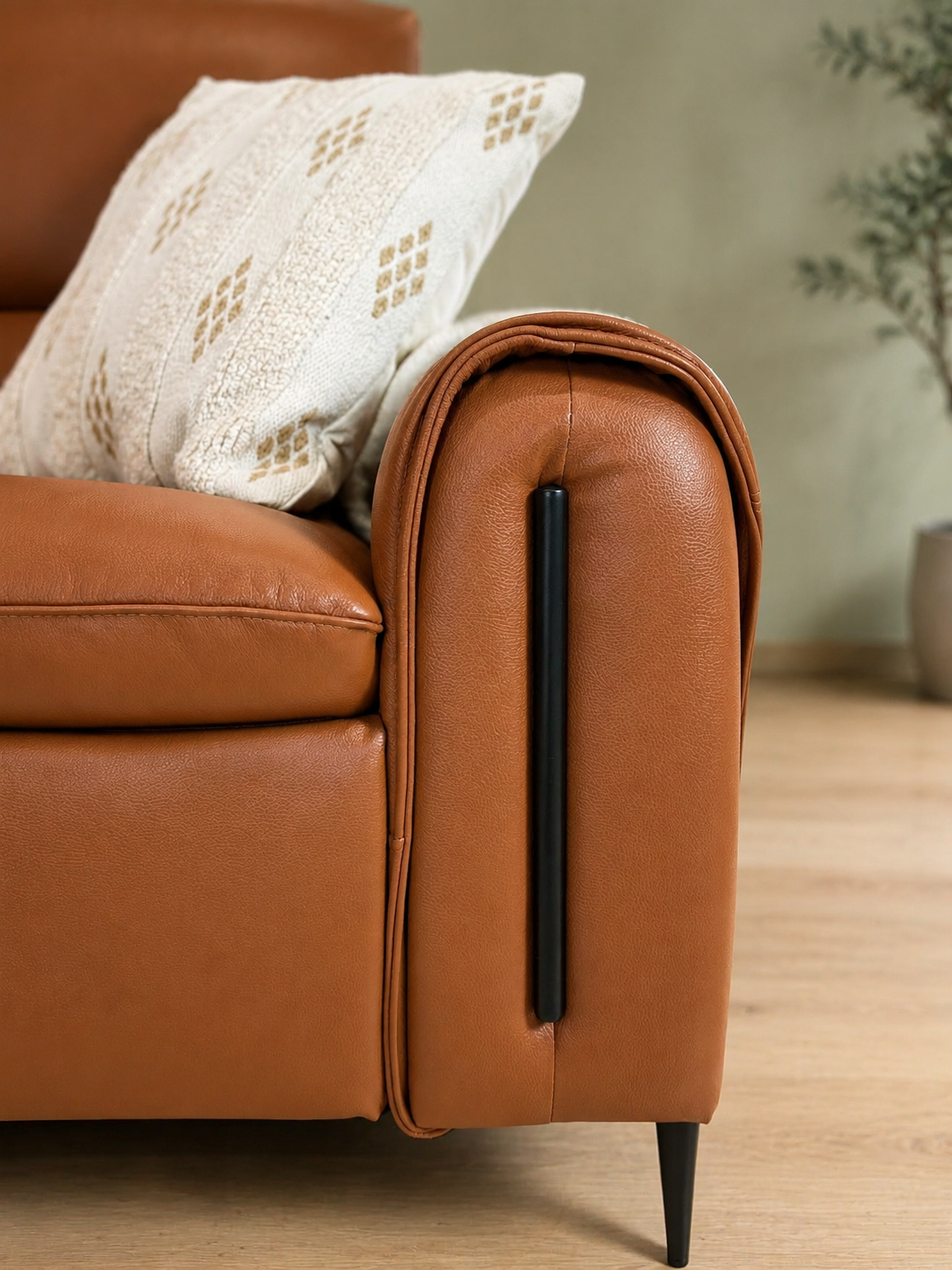 Close-up of a tan leather armchair corner with rolled armrests, in a softly lit room.