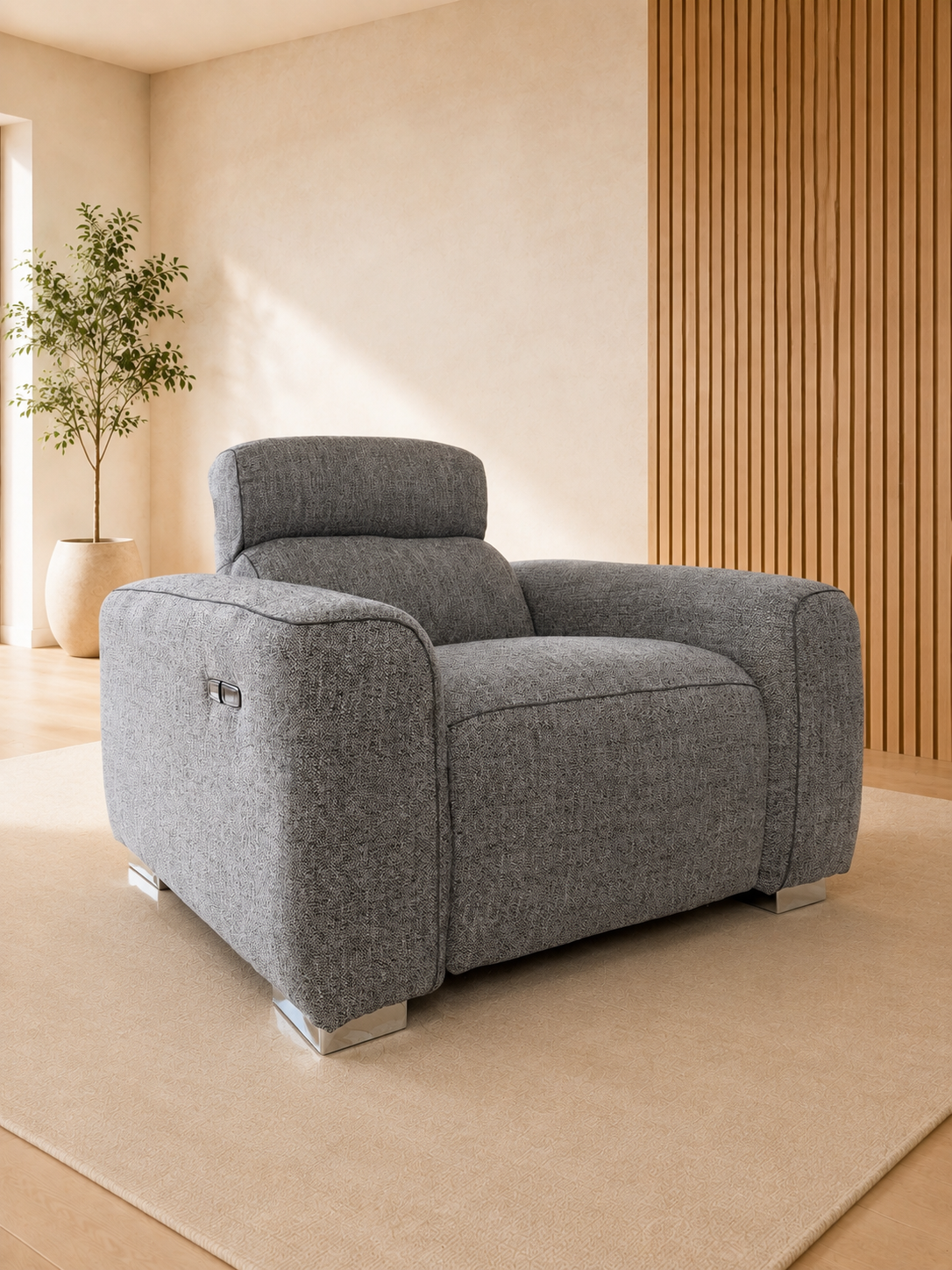 A modern gray upholstered armchair with a low, boxy silhouette and metallic silver legs, set on a beige rug in a minimalist room with a wood slat wall and a potted plant.