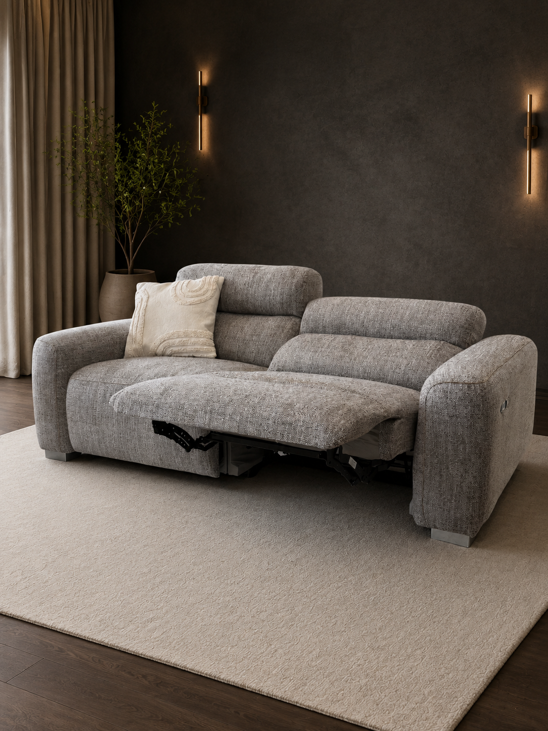 A modern gray fabric reclining sofa with a chaise lounge extended, styled in a contemporary living room with a beige rug, dark textured wall, and wall-mounted lights.