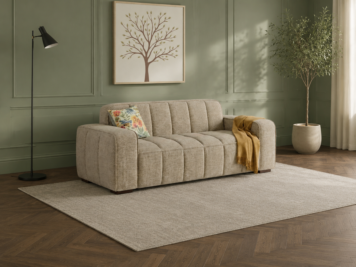 A modern tufted sofa in a light beige textured fabric, styled in a living room setting with a floral accent pillow, a mustard yellow throw blanket, a black floor lamp, a large area rug, and a potted tree against a sage green paneled wall.