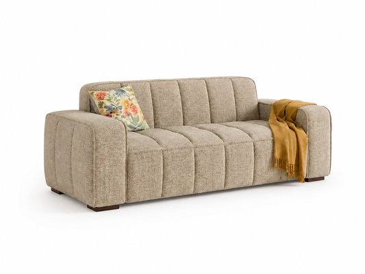 A modern three-seater sofa upholstered in a textured beige fabric, featuring a tufted backrest and armrests. A floral throw pillow and a mustard yellow throw blanket are styled on the sofa against a clean white background.