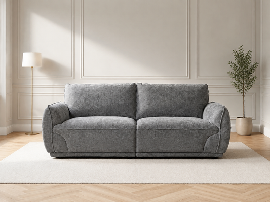 A modern two-seater sofa upholstered in textured gray fabric, styled in a minimalist living room setting with a white rug, a floor lamp, and a potted plant.