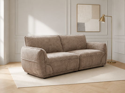 A two-seater loveseat sofa upholstered in a textured taupe fabric, styled in a bright, modern living room with a cream rug, wooden floor, gold floor lamp, and abstract wall art.