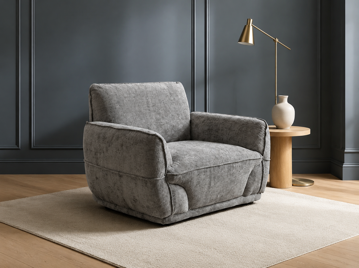 A modern gray upholstered armchair with a textured fabric, positioned on a light beige rug in a styled room with dark gray paneled walls, a wooden side table, a brass floor lamp, and a white ceramic vase.