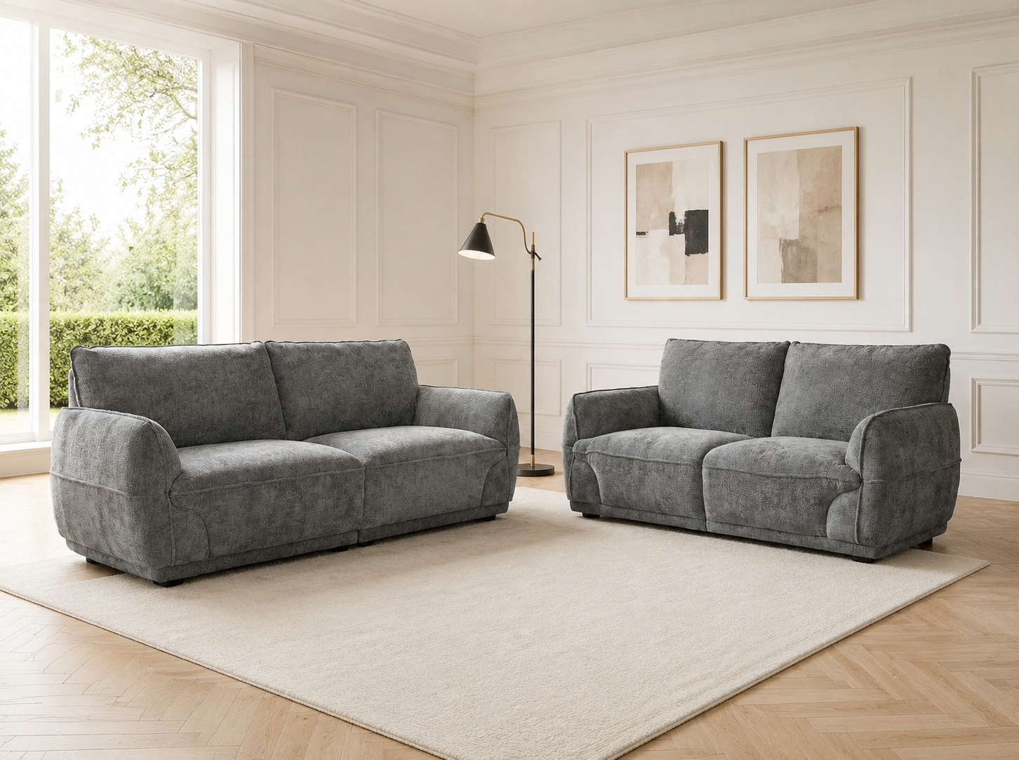 A gray upholstered loveseat and a matching armchair placed on a large cream rug in a bright, white-paneled living room with wood flooring and a floor lamp.