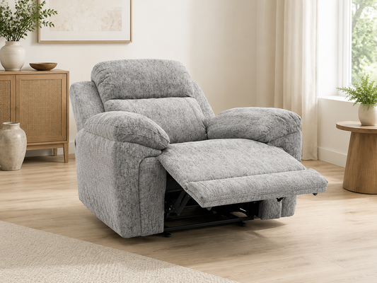 A plush gray upholstered recliner chair with the footrest extended, shown in a bright, modern living room with light wood floors, a side cabinet, and a window.