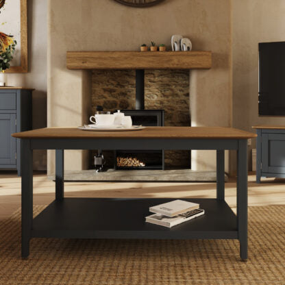 A rustic two-tone coffee table with a light brown wood top and a black metal frame, styled in a cozy living room in front of a fireplace.