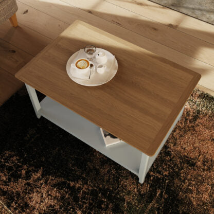 A rectangular coffee table with a light brown wood-grain top and white frame, shown in a room setting on a dark brown shag rug with wooden flooring in the background.