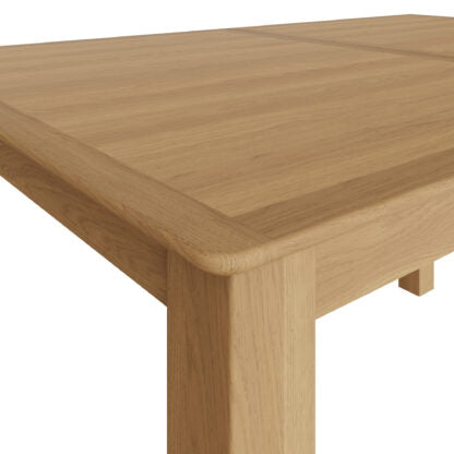 Close-up of a light oak wood table showing the tabletop grain, rounded corner, and front leg against a plain white background.