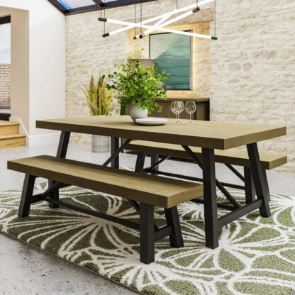 A rustic dining table set with two matching wooden benches, styled in a modern dining room with a patterned rug, brick wall, and pendant lights.