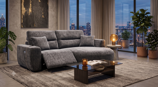 A modern gray upholstered reclining sofa in a styled living room with large windows showing a city skyline at dusk.