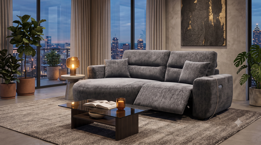 A modern gray upholstered reclining sofa in a styled living room with large windows showing a city skyline at dusk.