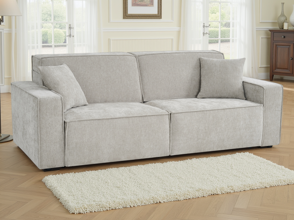 A light gray upholstered loveseat with two matching throw pillows, shown in a bright living room with wood flooring, a white shag rug, and windows in the background.