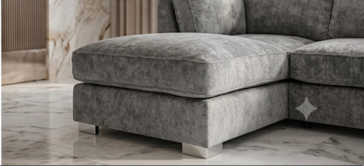 A close-up of a modern gray upholstered sectional sofa corner with a chaise-like extension, shown in a real interior setting with marble flooring and a marble wall panel.