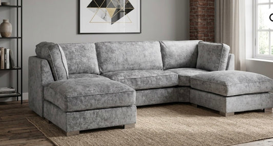 A light gray textured fabric sectional sofa with a left-facing chaise and a right-facing chaise, shown in a modern living room setting with a woven rug, brick wall, and window.