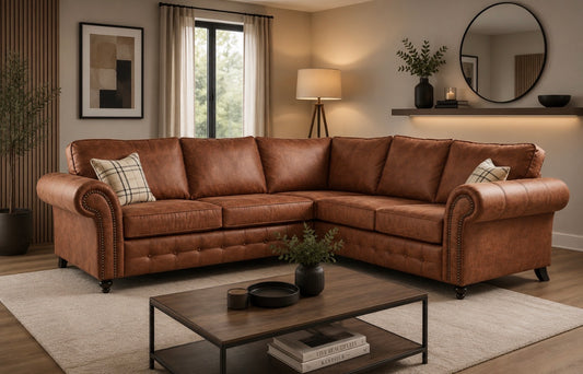 A brown leather sectional sofa with rolled arms and tufted detailing, styled in a modern living room with a coffee table, rug, and wall decor.