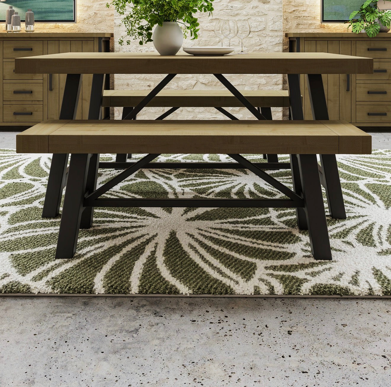 A rustic wooden dining table with matching bench set on a green and white patterned area rug in a dining room setting.
