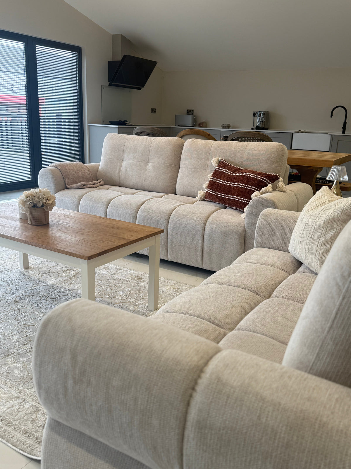 Beige sectional sofa in a living room with a wooden coffee table and kitchen in the background.