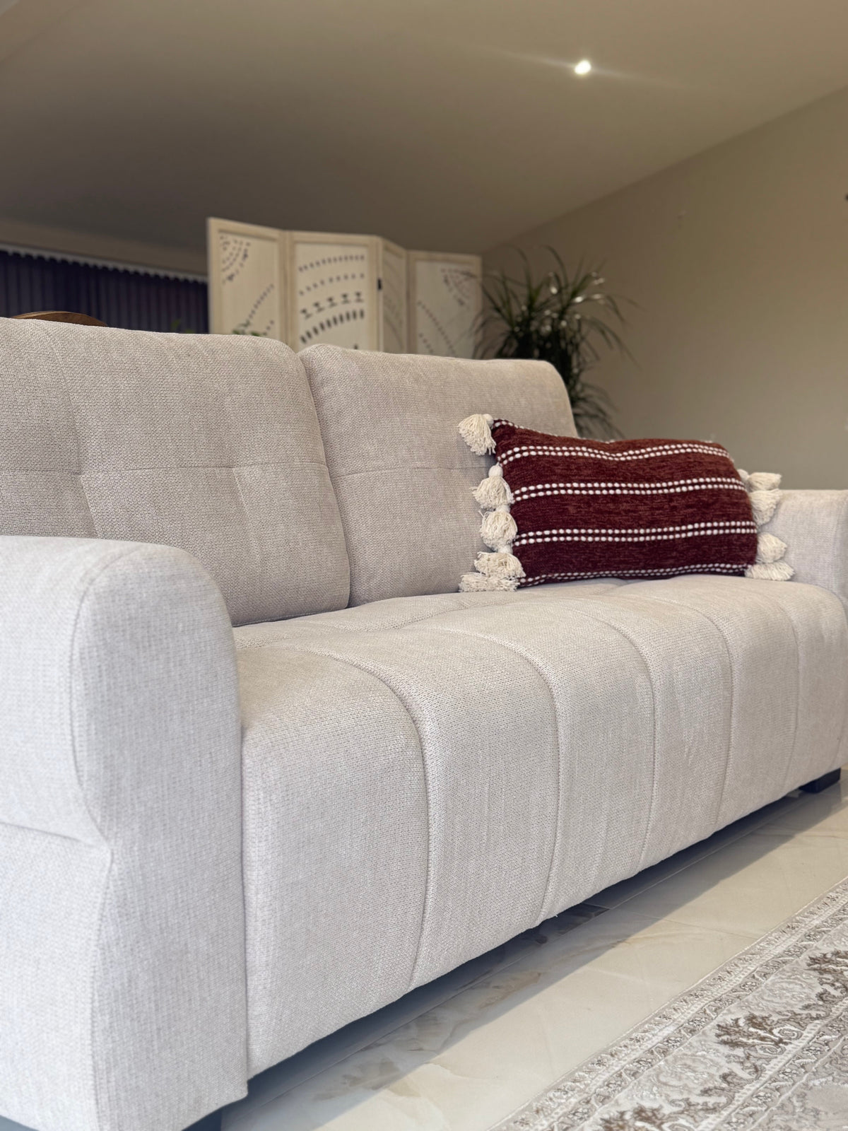 Beige sofa with a red and white patterned pillow in a living room setting.