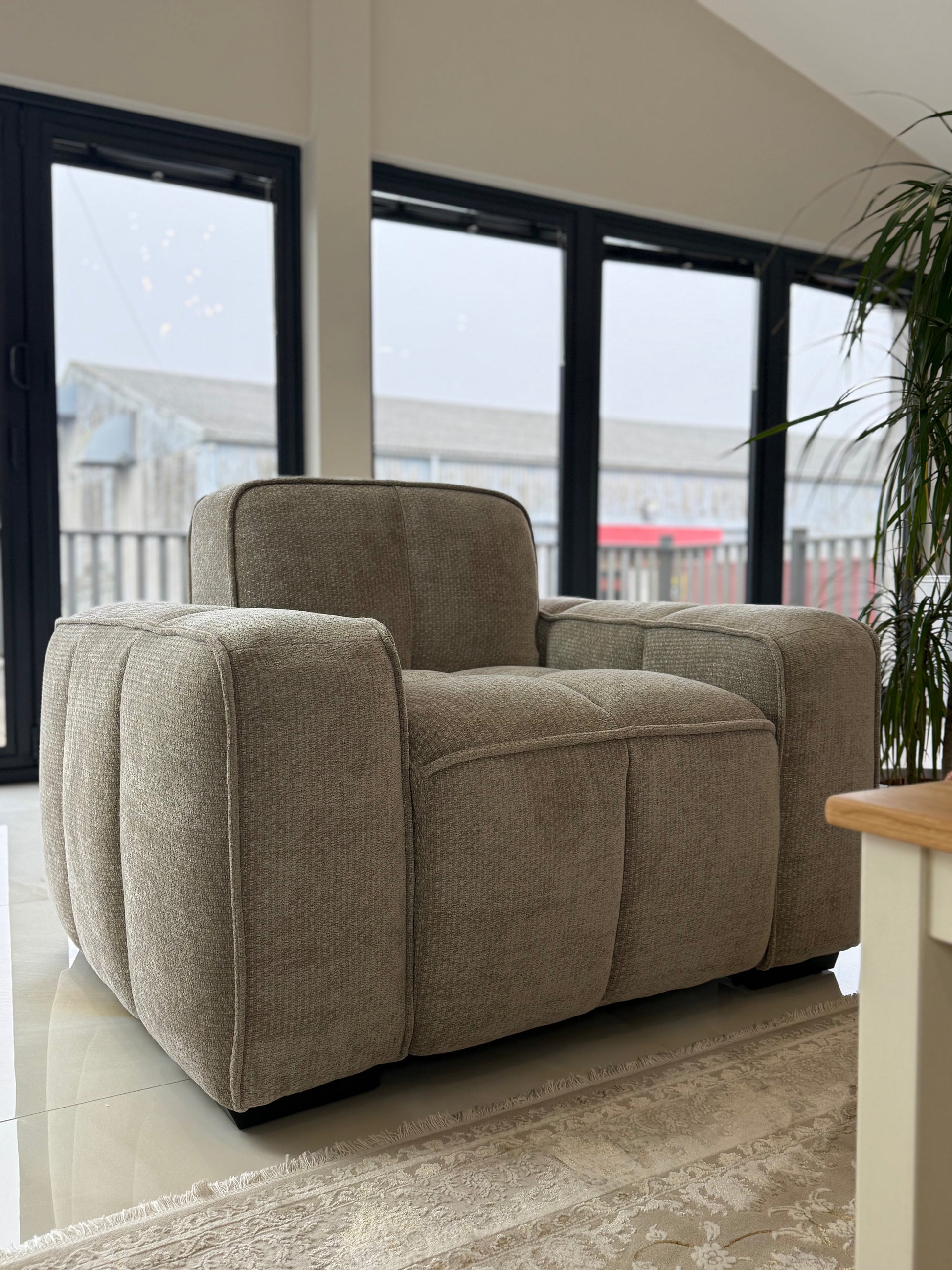 Beige armchair in a living room with large windows and a plant.