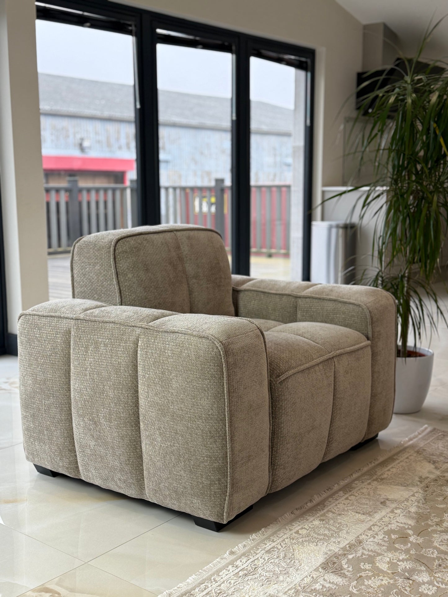 Beige armchair in a room with large windows and a plant.