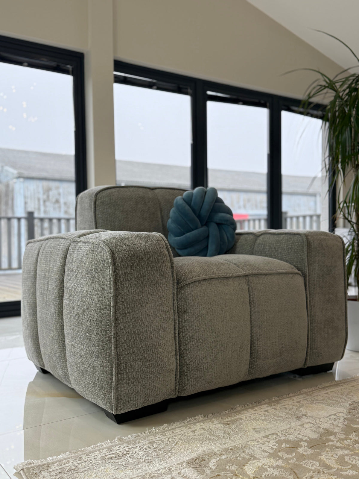 Gray armchair with a blue cushion in a room with large windows.