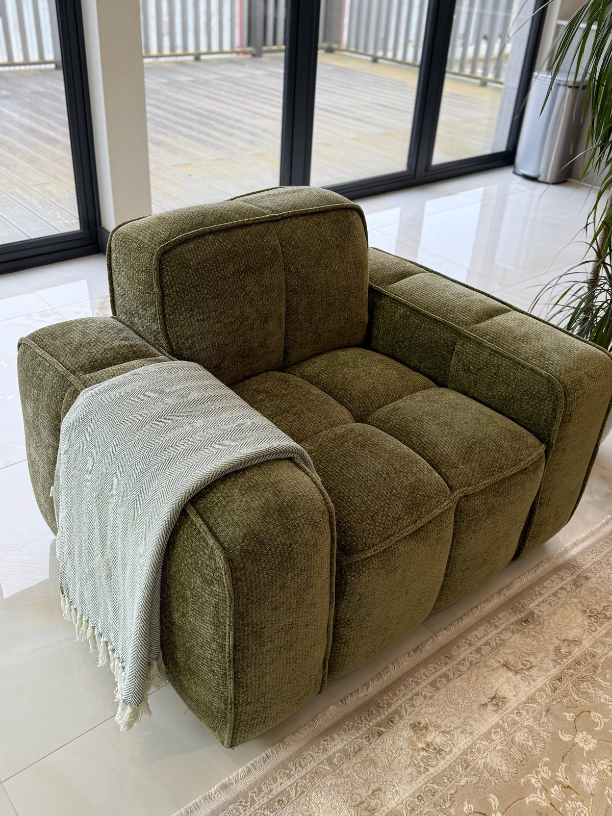Green armchair with a blanket in a room with large windows.