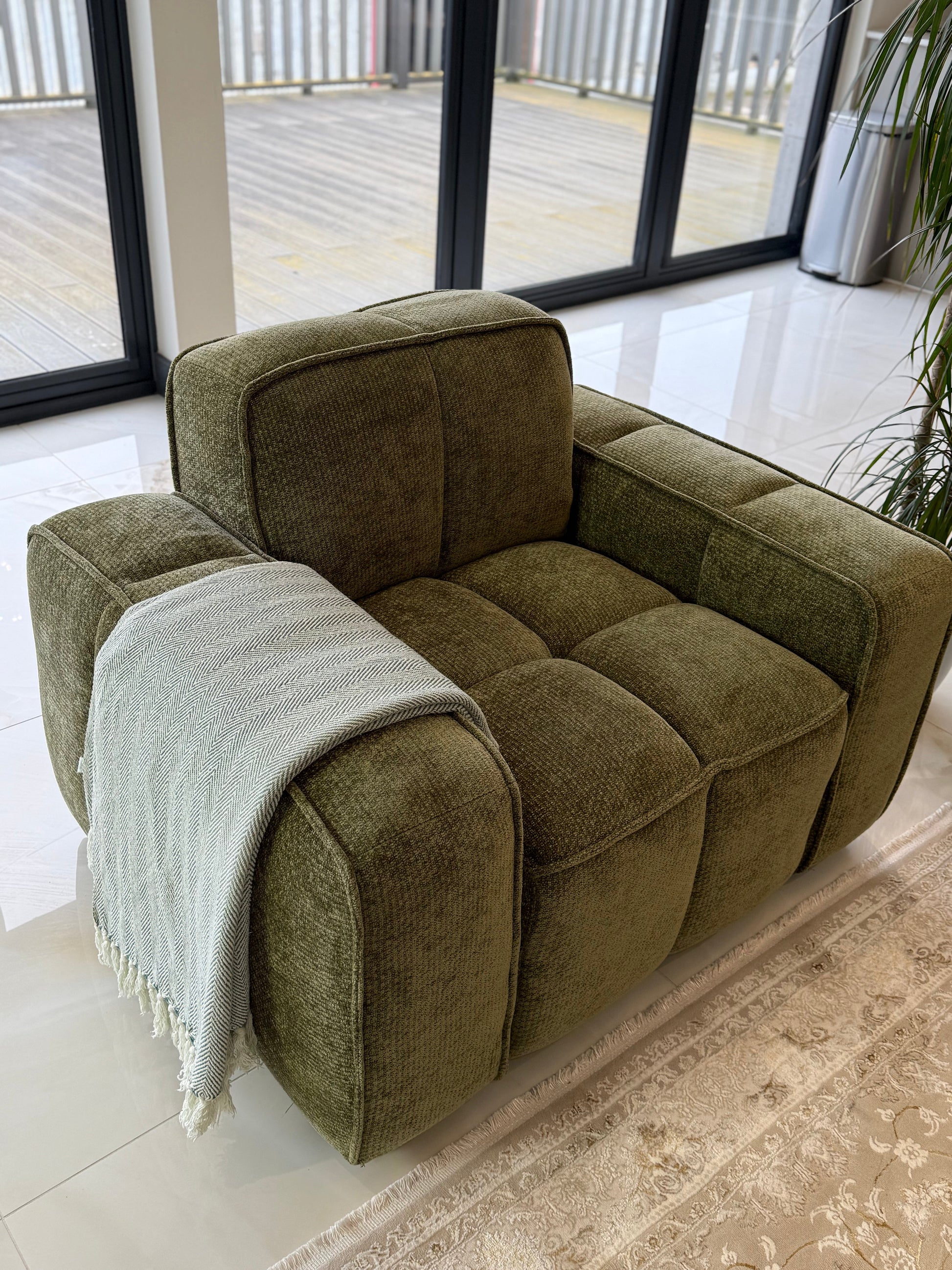 Green armchair with a blanket in a room with large windows.