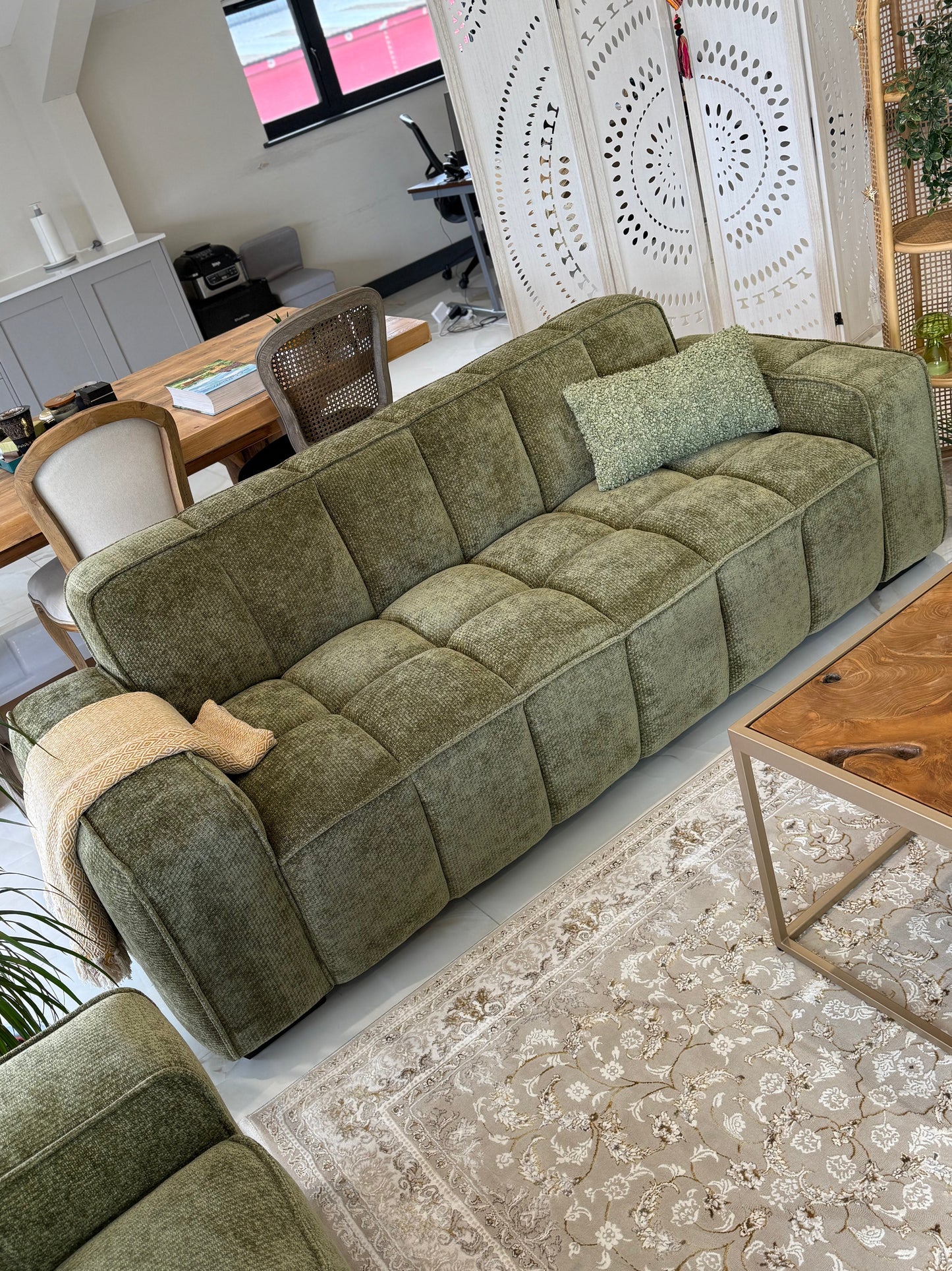 Green sofa in a living room with a dining area in the background