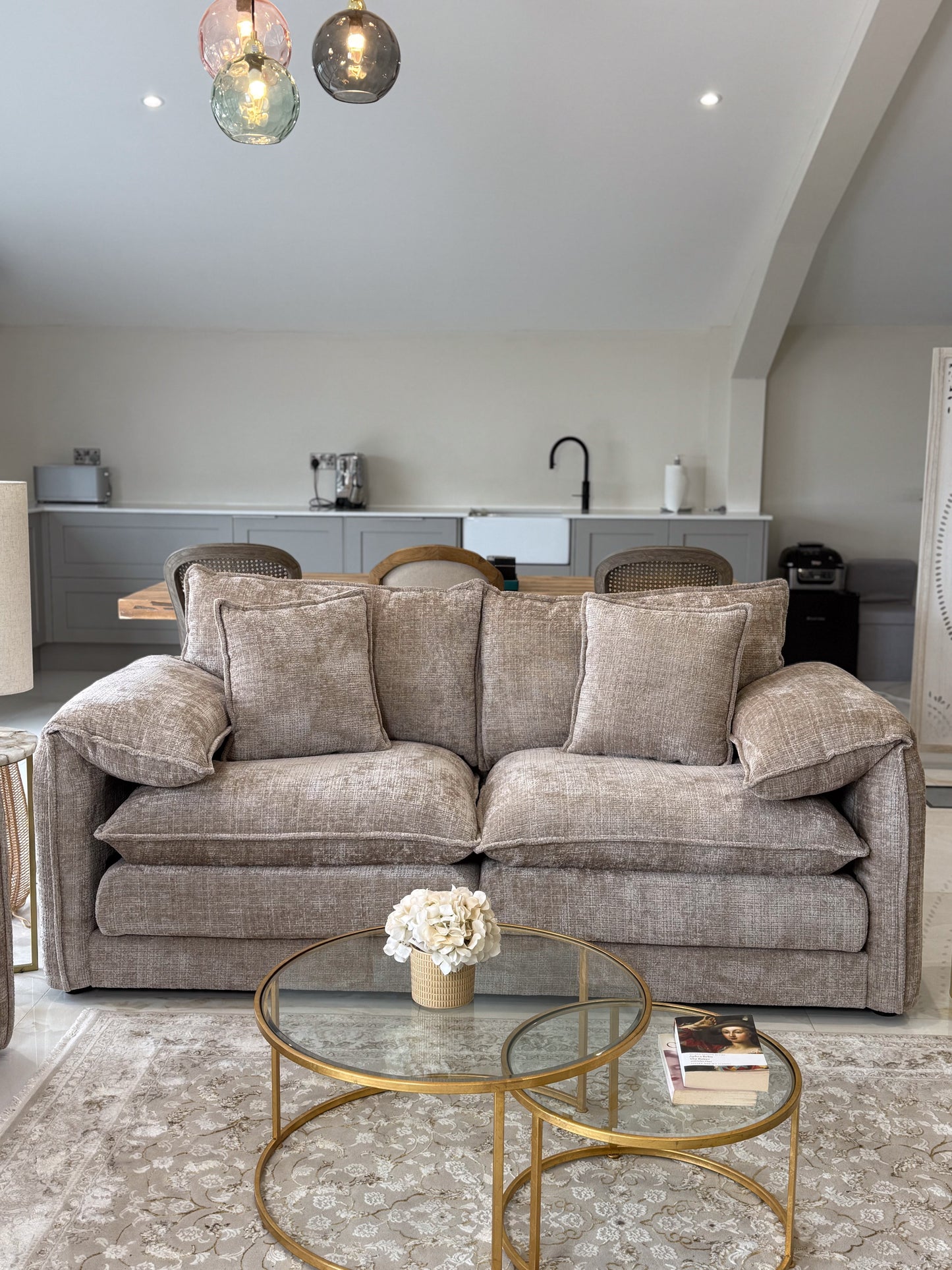 Living room with a beige sofa, glass coffee table, and kitchen in the background.