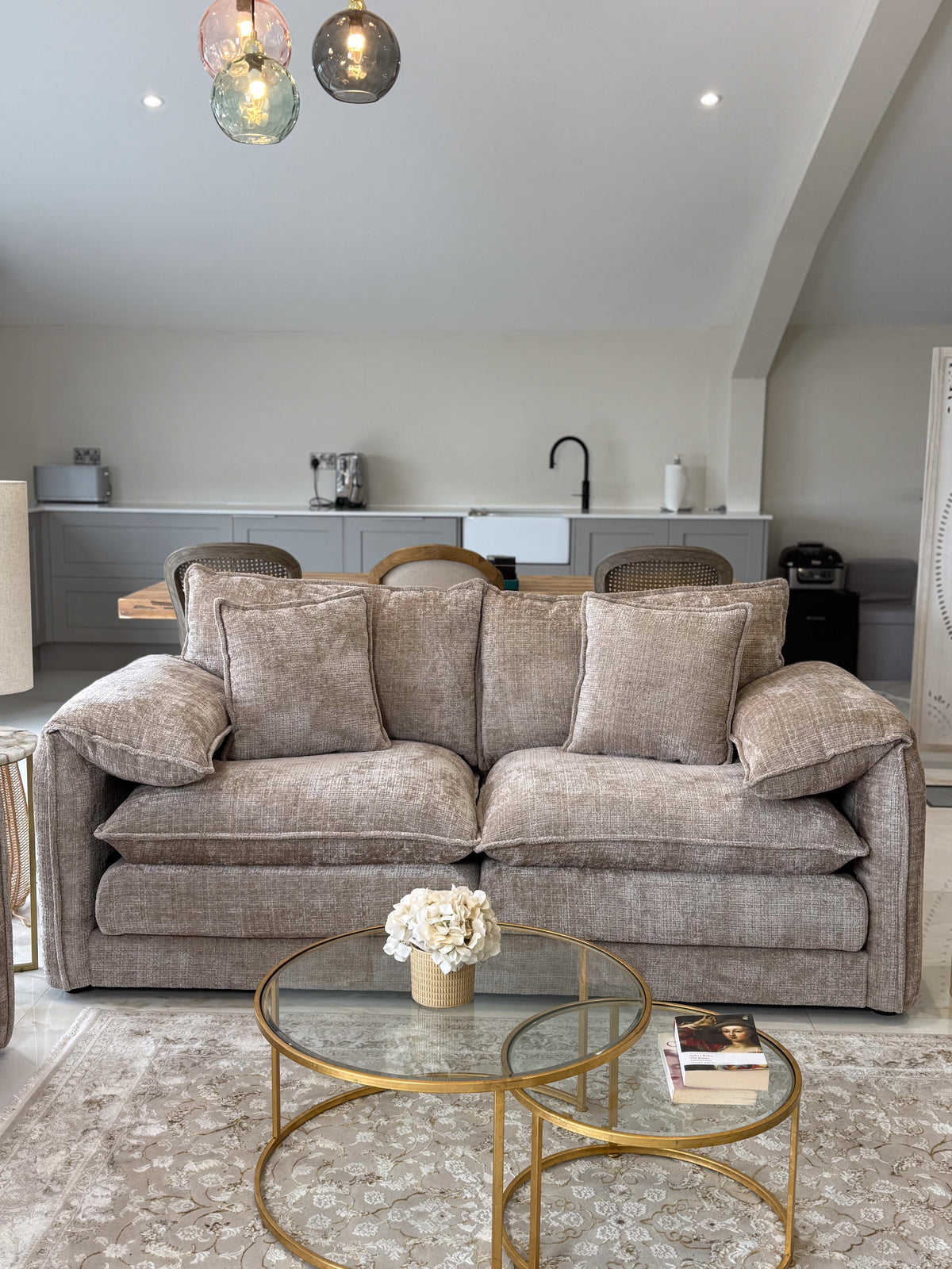 Living room with a beige sofa, glass coffee table, and kitchen in the background.